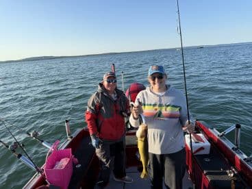 Two anglers on a fishing boat, with one proudly displaying a freshly caught Walleye. The serene lake setting enhances the fishing experience.
