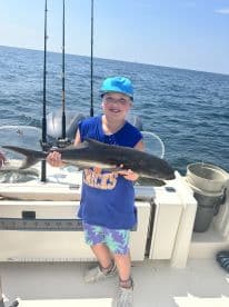 A young angler proudly displaying a caught fish while fishing on a boat in open waters.