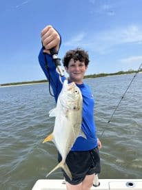 Young angler proudly holding a Jack Crevalle while fishing in a scenic coastal environment.