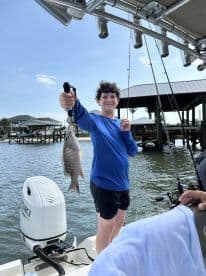 A young angler proudly displaying a Snapper caught while fishing from a boat in a coastal area.