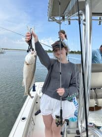 A young angler proudly displaying a large striped bass while fishing from a boat in a scenic waterway.
