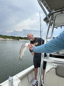 An angler proudly displaying a Redfish on a boat while enjoying a day of fishing in calm waters.