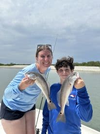 A mother and son proudly displaying their catch of two Snook while fishing in a calm coastal environment.