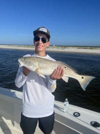 A young angler proudly displaying a Redfish while fishing from a boat in a coastal environment.