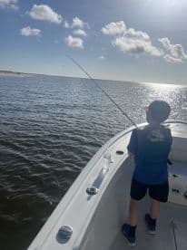 A young angler casting from the bow of a boat on a sunny day, enjoying a fishing adventure in calm waters.