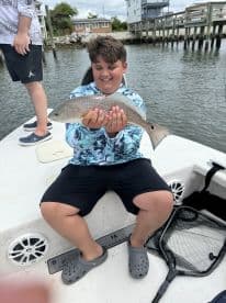 A young angler joyfully displaying a Redfish while sitting on a boat, showcasing a fun day of fishing.