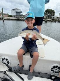 A young angler proudly displaying a Redfish while fishing from a boat, showcasing a fun family outing.