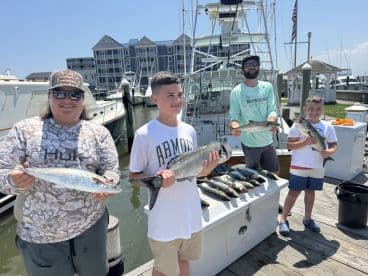 A family proudly displaying their catch of the day, featuring several fish including a large Spanish Mackerel, at the marina after a successful fishing trip.