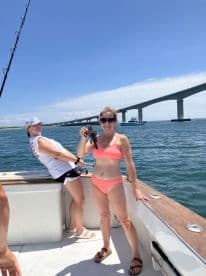 Two anglers enjoying a sunny day on the water, with one proudly displaying a caught fish near a bridge.