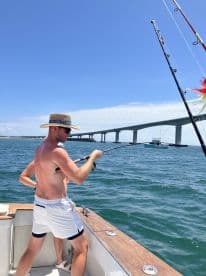 A fisherman reeling in a catch while enjoying a sunny day on the water near a bridge, showcasing the excitement of fishing.