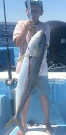 Young angler proudly holding a large fish while fishing on a boat in open waters.