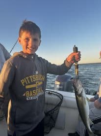 A young angler proudly displaying a freshly caught Walleye while fishing on a boat during sunset.