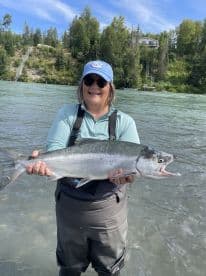An angler proudly displaying a large Silver Salmon while standing in a river, showcasing a successful fishing trip.
