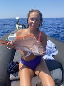 Angler displaying a large Snapper while seated on a boat in open water, showcasing a successful fishing trip.