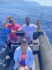 Group of friends enjoying a day on a fishing boat, with scenic ocean views in the background.