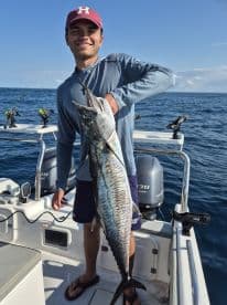 A young angler proudly displaying a large King Mackerel while fishing offshore, showcasing the excitement of a successful catch.