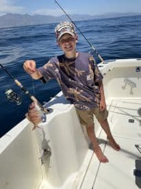A young angler proudly displaying a colorful Snapper while fishing on a boat in a scenic ocean setting.