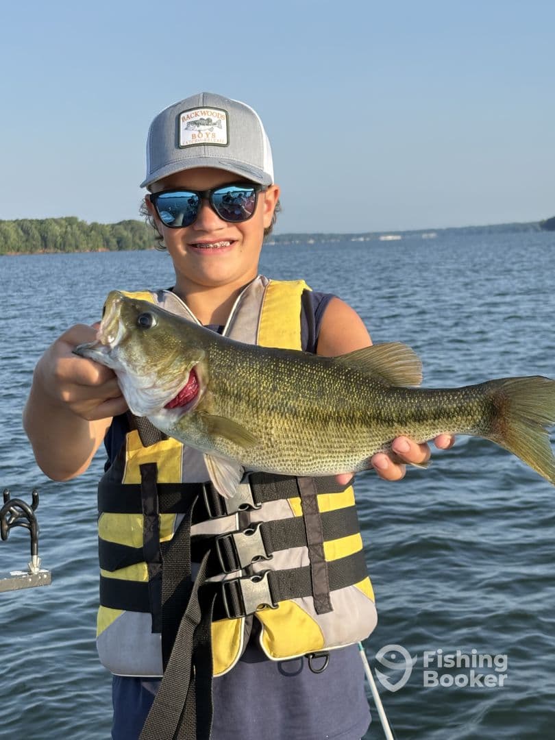 A young angler proudly displaying a large Largemouth Bass while fishing on a serene lake.