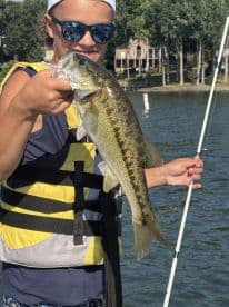 A young angler proudly displaying a large Largemouth Bass while fishing on a sunny day, showcasing a vibrant lake backdrop.