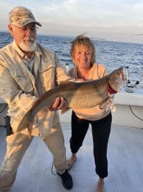Two anglers proudly displaying a large Lake Trout on a fishing boat, enjoying a successful day on the water.