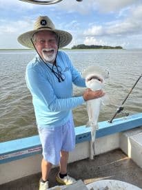 An angler proudly displaying a caught shark while fishing in a coastal waterway, showcasing a sunny day on the boat.