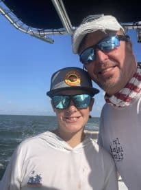 A smiling adult and a young angler pose for a selfie inside the boat, showcasing a fun day on the water.