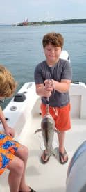 A young angler proudly displaying a caught fish while on a boat, enjoying a day of fishing.