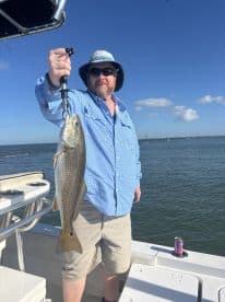 An angler proudly displaying a freshly caught Speckled Trout while aboard a fishing boat, enjoying a sunny day on the water.