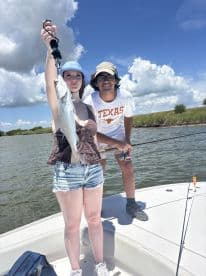 A young angler proudly displaying a Speckled Trout while fishing on a boat in a scenic coastal environment.