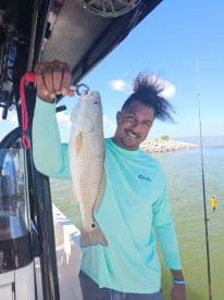 An angler proudly displaying a large Redfish while fishing from a boat in a coastal environment.