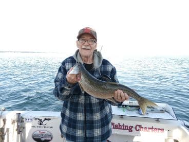 An elderly angler proudly displaying a large Lake Trout while fishing on a charter boat.
