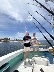 Two young anglers proudly displaying their catch, a Mahi Mahi and a King Mackerel, aboard a fishing boat in a coastal setting.