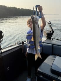 A young angler proudly displaying a large Lake Trout while fishing on a serene lake, showcasing a memorable moment on the water.
