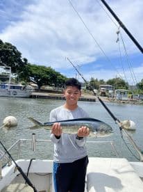 Young angler proudly holding a Mahi Mahi on a boat after a successful fishing trip.