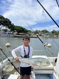 A young angler proudly displaying a large Mahi Mahi aboard a fishing boat, showcasing a successful day on the water.