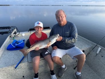 A young angler and an adult proudly displaying a large Redfish on a calm water fishing trip.
