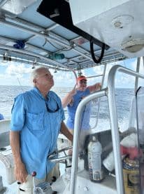 Two anglers navigating the boat's helm, enjoying a day on the water with clear skies and a calm sea.