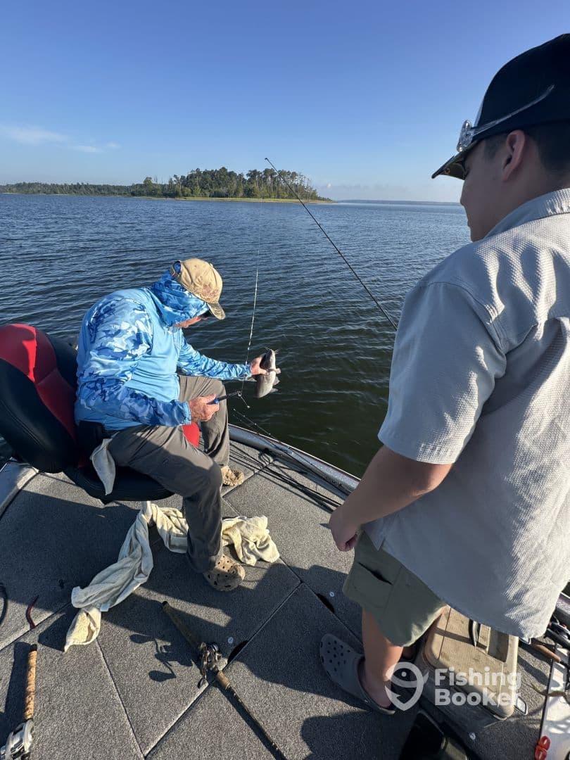 A young angler watches as an adult prepares to release a freshly caught fish while fishing on a calm lake.