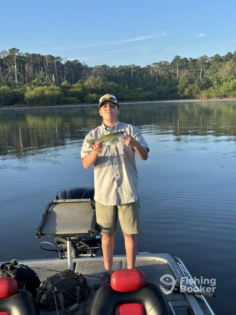 A young angler proudly displaying a Bass while fishing on a calm lake during early morning.