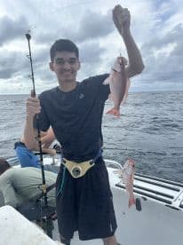 A young angler proudly displaying two Red Snapper caught during a fishing trip on a boat.