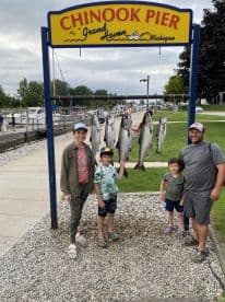 A family poses proudly in front of a catch board displaying several Chinook Salmon at Chinook Pier in Grand Haven, Michigan.