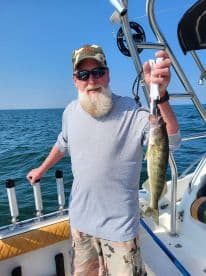 An angler proudly displaying a Walleye while fishing on a boat in clear waters.