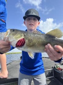 Young angler proudly displaying a large Largemouth Bass while fishing on a boat.