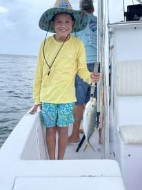 A young angler proudly displaying a caught fish while enjoying a fishing trip on a boat.