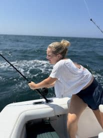 A young angler actively reeling in a fish while fishing on a boat in open waters, showcasing the excitement of the sport.