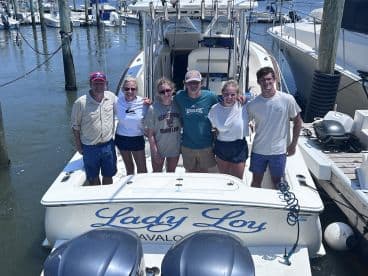 A cheerful group of anglers posing on the deck of the 'Lady Loy' boat at the marina, ready for a day of fishing.