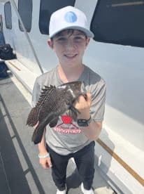 A young angler proudly displaying a Black Sea Bass while fishing on a charter boat.