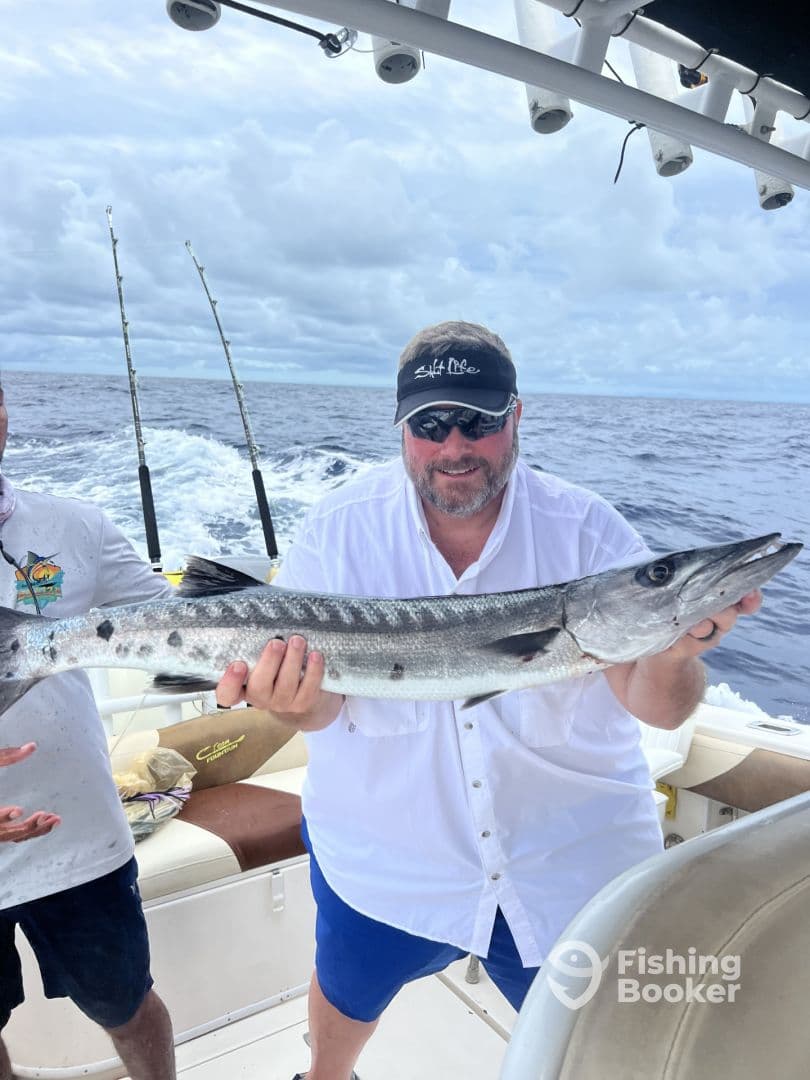 An angler proudly displaying a large Barracuda while aboard a fishing boat in open waters.