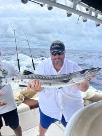 An angler proudly displaying a large Barracuda while aboard a fishing boat in open waters.