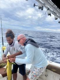 Two anglers working together to secure a vibrant Mahi Mahi on a sport fishing boat, showcasing teamwork during a deep-sea fishing adventure.